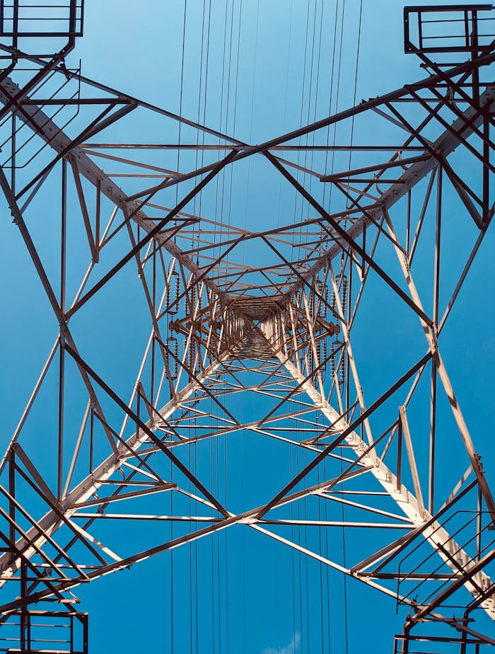 A vertical perspective of a steel power transmission tower against a clear blue sky in Tokyo, Japan.