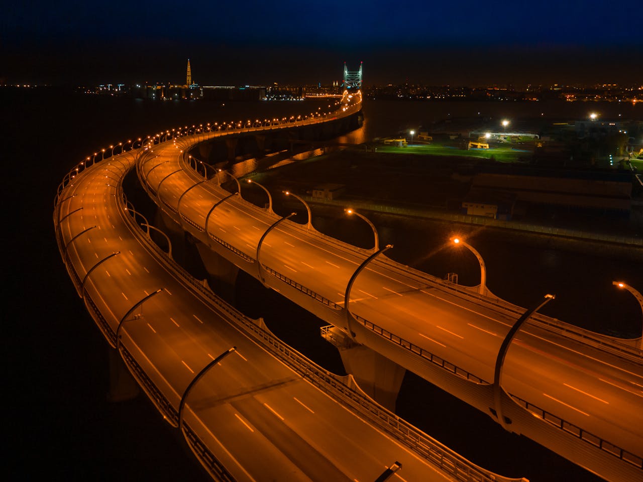 Aerial view of a winding city bridge at night with glowing lights and urban skyline.